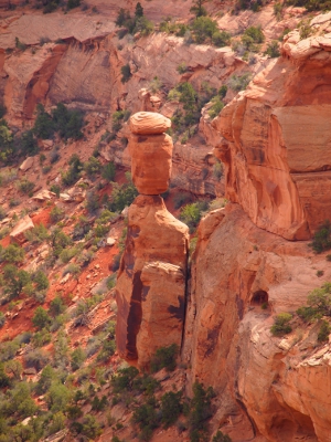 [A cylindrical rock which appears separate from and perched on another rock below it. Top rock is at least 100 feet above the ground. Both rocks are within the canyon.]